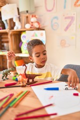 Beautiful african american toddler sitting painting car toy using marker pen on desk at kindergarten