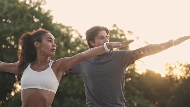 Strong couple in sportswear man and woman in tracksuits doing yoga exercises together while working out at playground outdoors