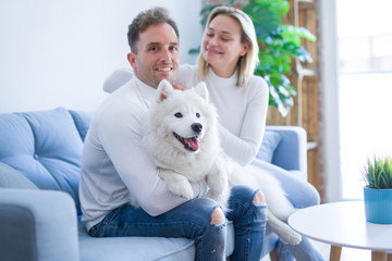 Young beautiful couple with dog sitting on the sofa at new home around cardboard boxes