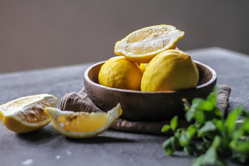 Photo of fresh ripe lemons on dark background. A slice of lemon with green leaves. Lemon fruit on wooden plate bowl. Copy space. Retro background. Image