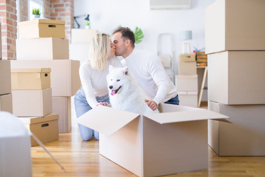 Young beautiful couple with dog kissing sitting on the floor at new home around cardboard boxes