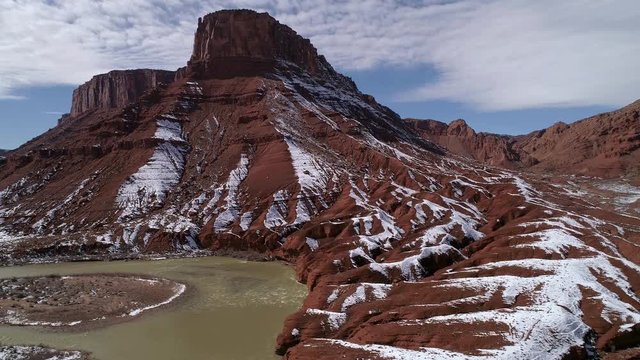 Panning aerial view of red earth landscape with snow melting along the Colorado River in the Utah desert.