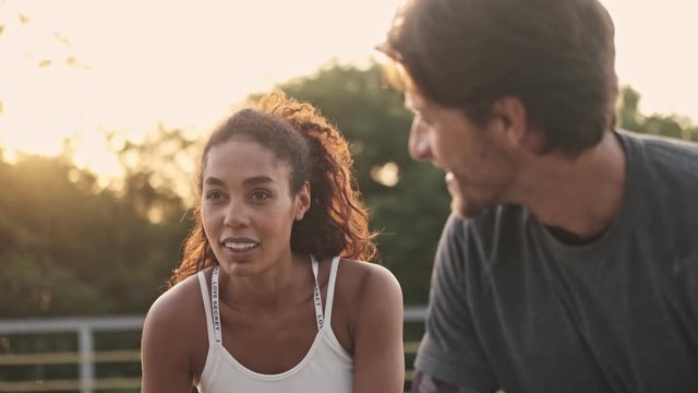 Calm couple man and woman in sportswear looking at each other while resting during workout at playground outdoors