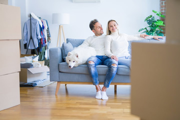 Young beautiful couple with dog sitting on the sofa at new home around cardboard boxes