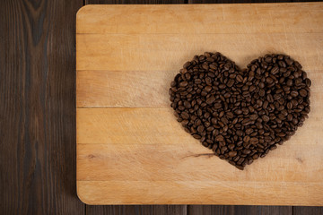 A heart of coffee beans on a wooden background of beige blossomed. Concept of love, holiday, Valentine's day, international women's day.