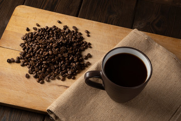 A grain of brown coffee on a wooden background of beige blossomed with a Cup filled with coffee.