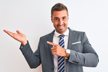 Young handsome business man wearing suit and tie over isolated background smiling cheerful presenting and pointing with palm of hand looking at the camera.