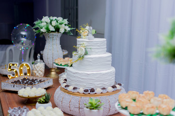 A beautiful cake for the 50th anniversary decorated. Table birthday party whith a two-tier white cake decorated with yellow roses and green leafy branches. Selective focus. festive concept.