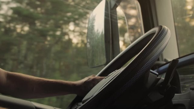 Man holding his hands on steering wheel and driving car at country road on warm summer day. Truck driver rides to destination.  View from the lorry cab. 