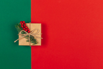 Craft gift box with spruce branch and red berries on green and red background. Holiday eco-friendly concept.