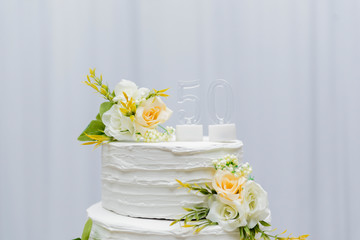 A beautiful cake for the 50th anniversary decorated. Table birthday party whith a two-tier white cake decorated with yellow roses and green leafy branches. Selective focus. festive concept.
