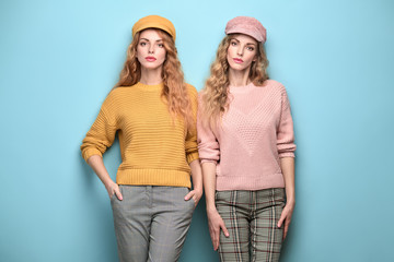 Fashionable woman in stylish outfit, makeup posing on blue. Two Beautiful blonde redhead girl, trendy pink yellow jumper, cap, fashion hair. Adorable sister friend, colorful pastel concept