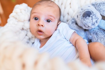 Adorable baby lying down over blanket on the floor at home. Newborn relaxing and resting comfortable with teddy bear