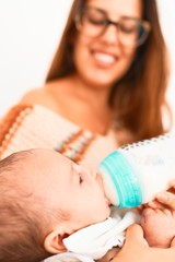 Young beautiful woman and her baby on the sofa at home. Newborn and mother relaxing and resting comfortable drinking milk using feeding bottle