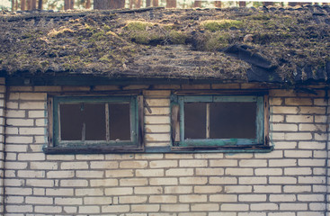 Old brick building with broken windows and a roof overgrown
