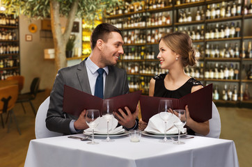 leisure and luxury concept - smiling couple with menus over restaurant or wine bar background