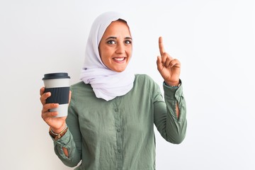 Young beautiful Arab woman wearing traditional Muslim hijab drinking a coffee surprised with an idea or question pointing finger with happy face, number one