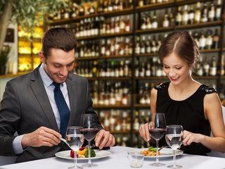 leisure and luxury concept - smiling couple eating main course over restaurant or wine bar background