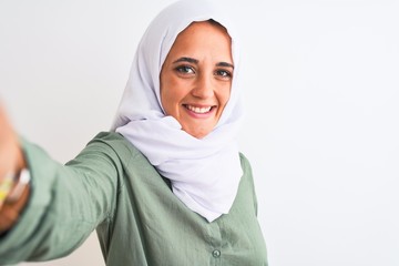 Young Arab woman wearing hijab taking selfie photo over isolated background with a happy face standing and smiling with a confident smile showing teeth