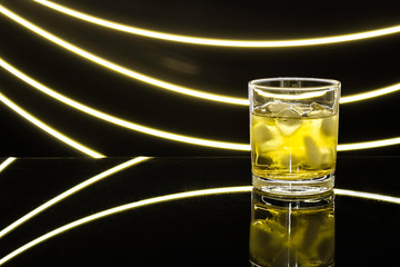 Glass misted glass with a drink and ice on a transparent dark table, the glare of light, drawing light. Free space for text. Glass of whiskey, brandy