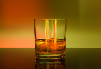 Glass whisky glass with ice in green-orange light