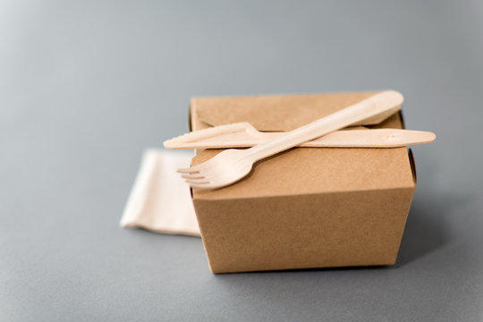 package, recycling and eating concept - disposable box for takeaway food with wooden fork, knife and napkin on table