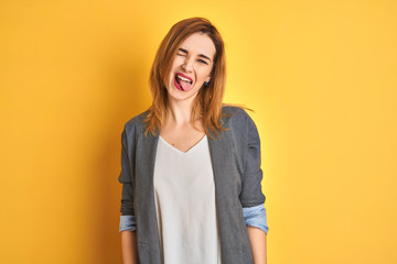 Redhead caucasian business woman over yellow isolated background sticking tongue out happy with funny expression. Emotion concept.