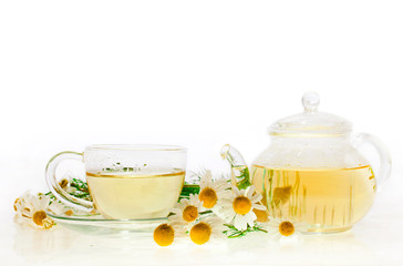 Herbal tea with chamomile flowers in a glass cup and teapot isolated on white background
