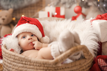 Cute little baby with Santa Claus hat lying in basket at home