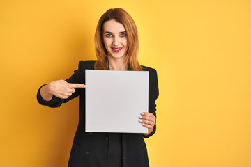 Naklejka premium Young redhead businesswoman with clear eyes holding banner over isolated yellow background very happy pointing with hand and finger