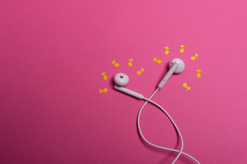 white earphones and yellow paper notes on pink background. view from above.