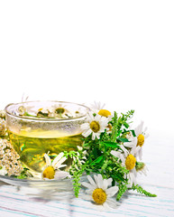 Herbal tea with chamomile and common yarrow in a glass cup with fresh herbs on white wooden background