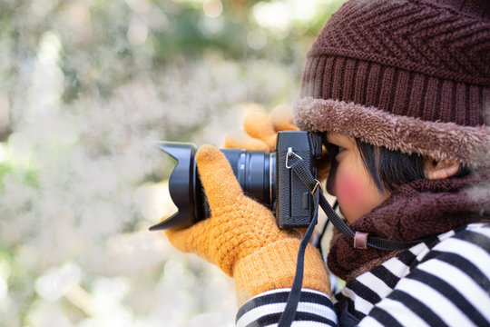 Portrait of a cute little girl in Wool hat taking a picture with digital camera at the weather is cold on blurred background
