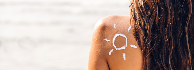 Woman wearing two piece bikini applying suncream with sun drawn on back on the tropical...