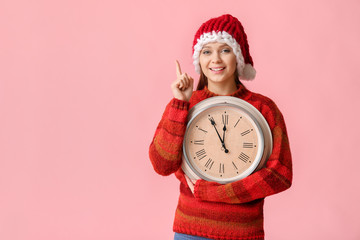 Young woman in Santa hat and with clock on color background. Christmas countdown concept