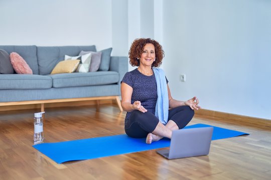 Middle age beautiful sportswoman smilig happy. Sitting on mat with smile on face using laptop at home