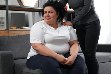 Woman comforting her depressed overweight friend at home