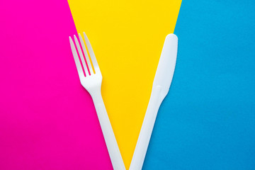 Plastic white fork and knife on multicolored background. Cooking utensil. Top view. Minimalist Style. Copy, empty space for text