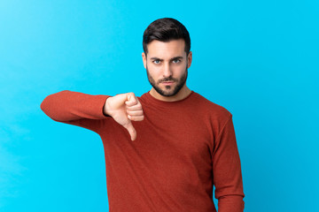 Young handsome man with beard over isolated blue background showing thumb down sign