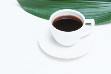 White cup of black coffee and green leaf on a white background.