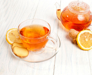 Glass cup of tea with ginger and lemon on a white wooden background.