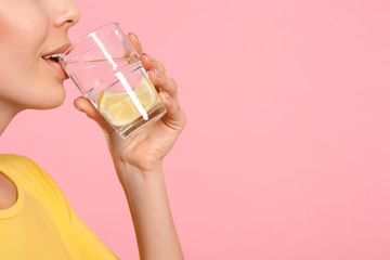 Young woman drinking tasty lemon water on pink background, closeup. Space for text