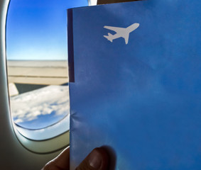 Sitting by window on a plane with magazine in hands.