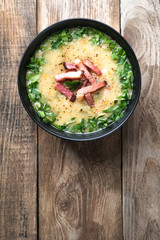 Pea soup with bacon, herbs and bread crumbs in a black bowl on a rustic background top view copy space.