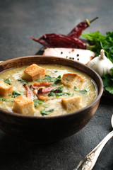 Pea soup with bacon, herbs and bread crumbs in rustic bowl on a dark background.