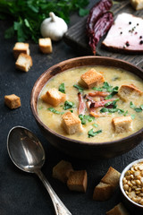 Pea soup with bacon, herbs and bread crumbs in rustic bowl on a dark background.