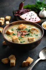 Pea soup with bacon, herbs and bread crumbs in rustic bowl on a dark background.