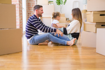 Beautiful family sitting on the floor playing with his kid at new home around cardboard boxes