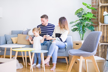 Beautiful family, parents sitting on the sofa drinking coffee looking his kid playing at new home around cardboard boxes