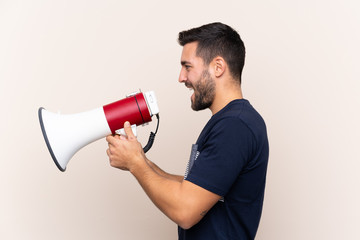 Young handsome man with beard over isolated background shouting through a megaphone